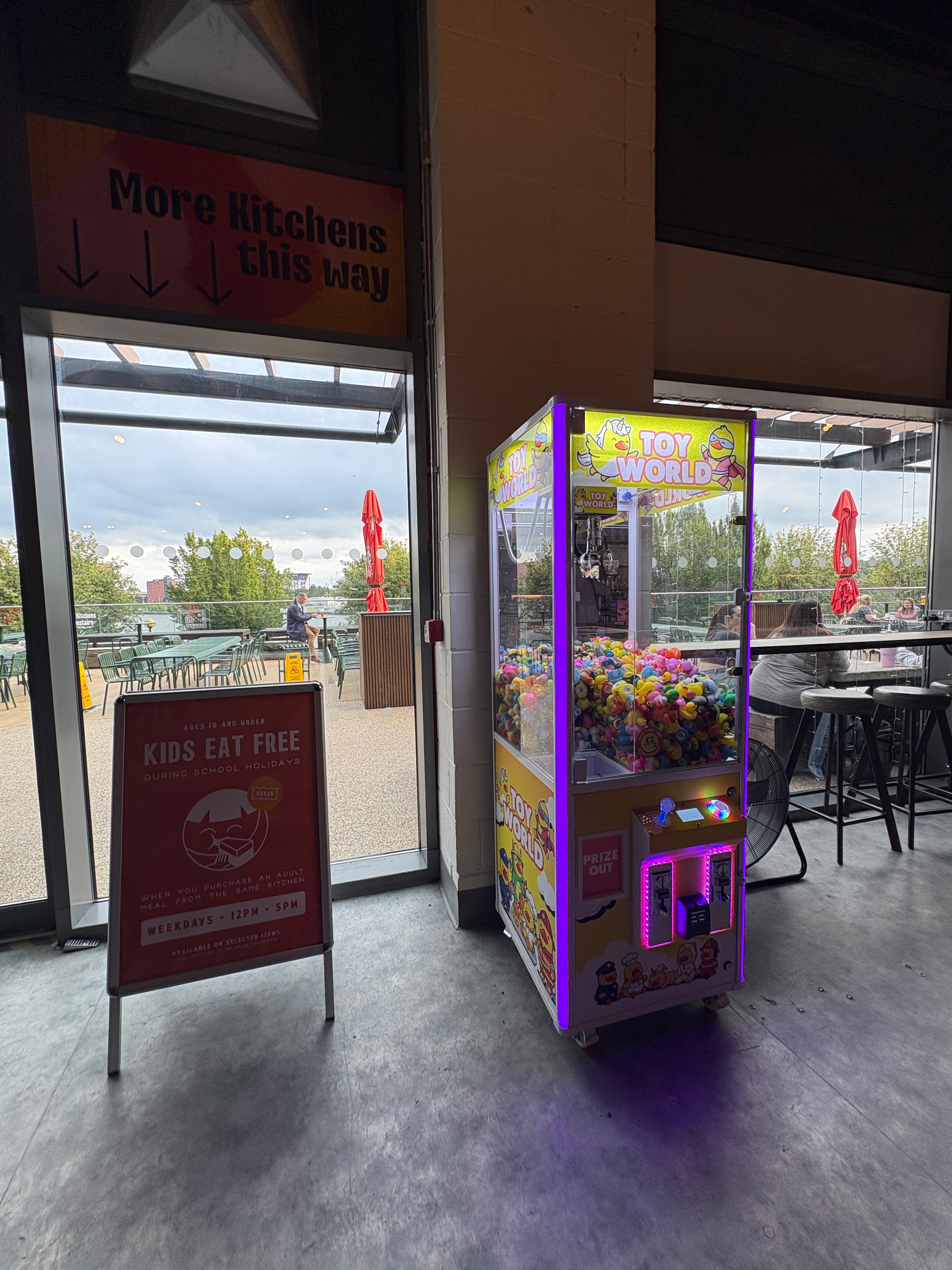 A Toy World claw machine near a restaurant entrance